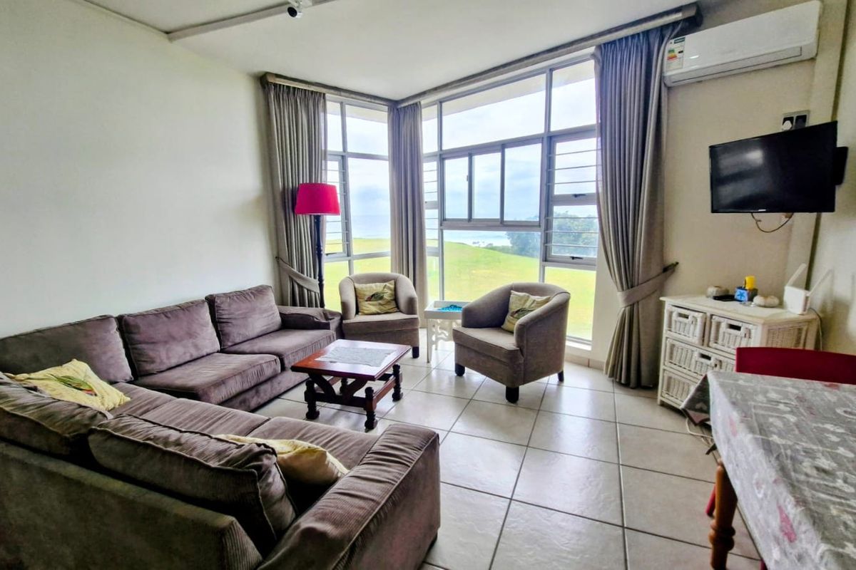 A bright living room featuring large windows with scenic views, tiled flooring, and a wall-mounted air conditioning unit.