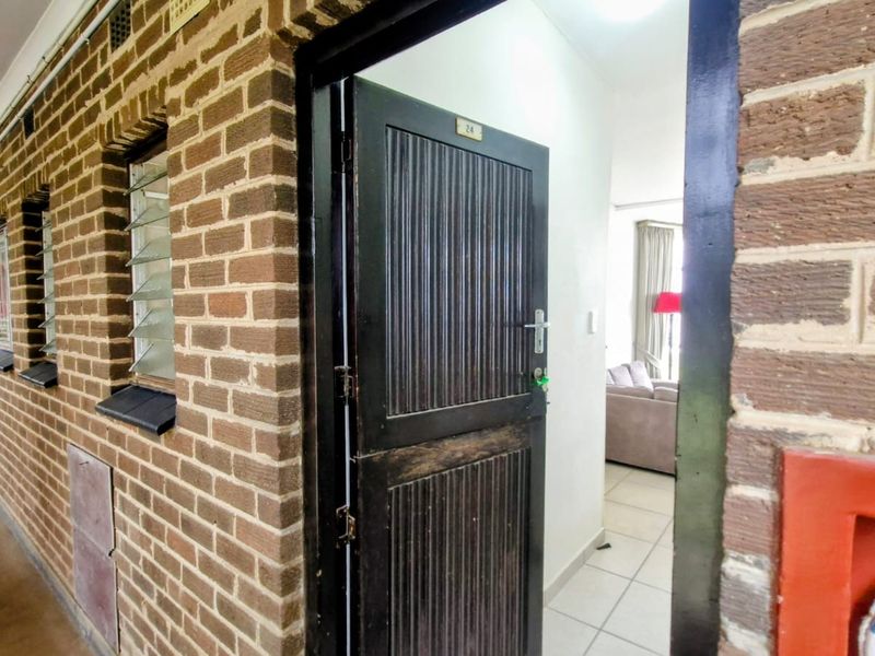 Exterior view of an apartment entrance featuring a brick facade, louvre windows, and a direct view into the tiled interior living space.