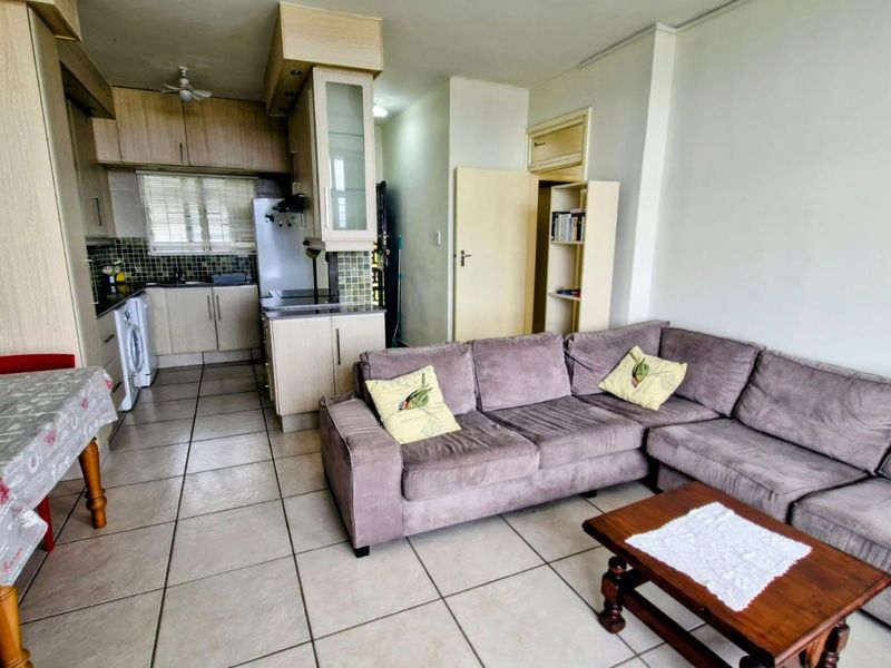 Open-plan living area featuring a functional kitchen with built-in cabinetry and tiled flooring, seamlessly connected to the lounge space.