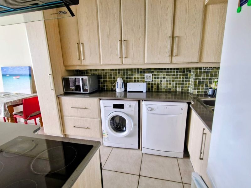 A functional kitchen featuring light wood-grain cabinetry, mosaic tile backsplash, stone countertops, and integrated appliances including an electric hob and extractor fan.