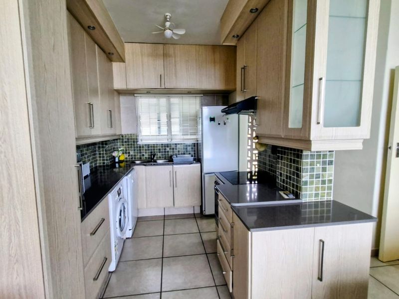 A functional kitchen featuring light wood-finish cabinetry, dark stone countertops, a mosaic tile backsplash, and tiled flooring with integrated appliance spaces.