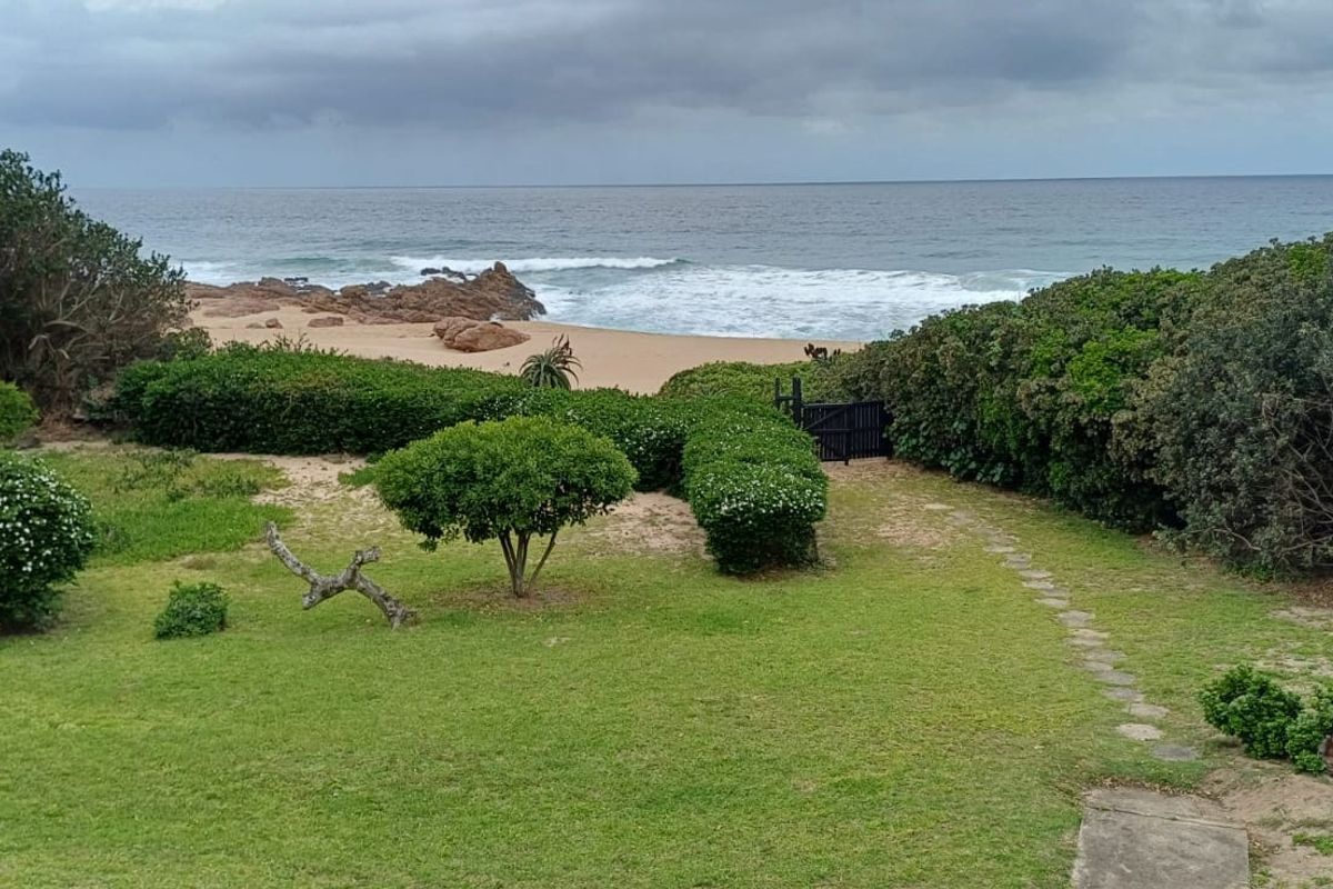 A scenic view of a lush garden leading directly to a sandy beach and the ocean, featuring established landscaping and a private gate.