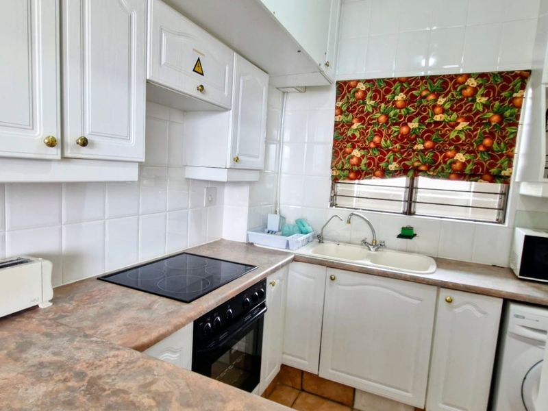 Compact kitchen featuring white cabinetry, a built-in electric hob and oven, tiled splashbacks, and a double basin sink.