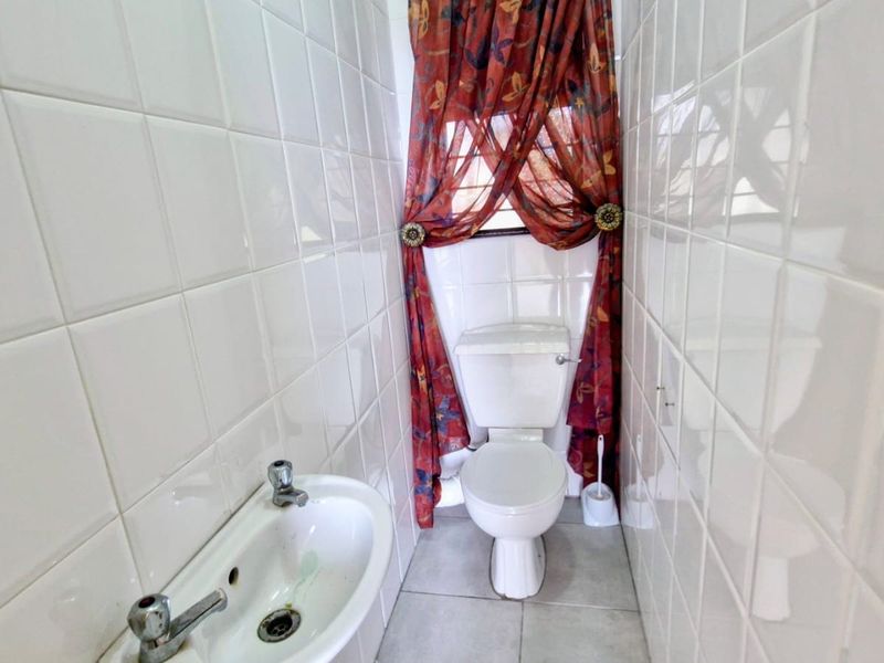 A compact bathroom featuring floor-to-ceiling white wall tiles, a pedestal sink, and a standard toilet.