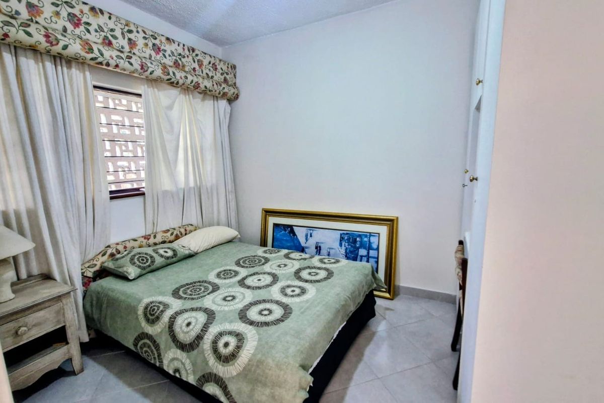 A bedroom featuring tiled flooring and a window with built-in security bars, offering a functional space with neutral wall finishes.