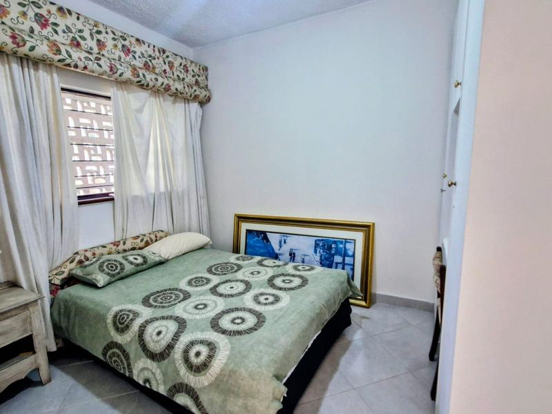 A bedroom featuring tiled flooring and a window with built-in security bars, offering a functional space with neutral wall finishes.