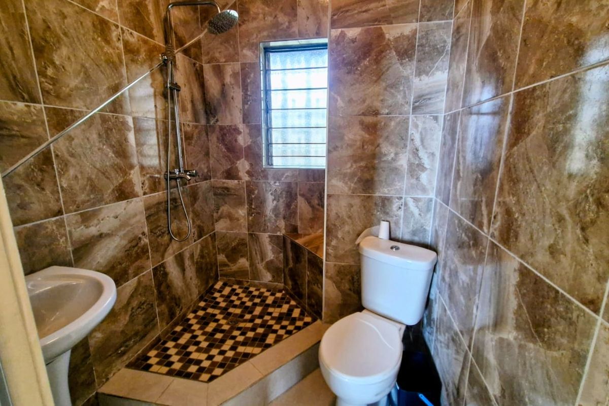 A compact bathroom featuring floor-to-ceiling brown marble-effect tiles, a corner shower enclosure with a mosaic tile floor, a pedestal basin, and a toilet.