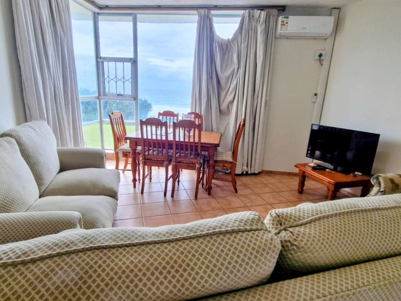 Open-plan living and dining area featuring tiled flooring, wall-mounted air conditioning, and large windows with ocean views.