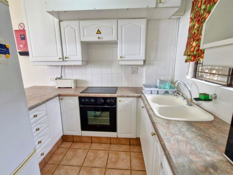 A functional kitchen featuring white cabinetry, a built-in oven with a glass cooktop, double basin sink, and tiled flooring.