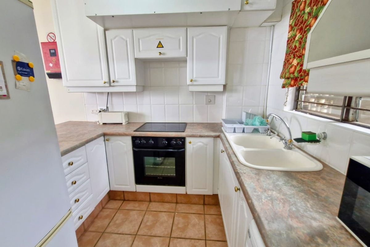 A functional kitchen featuring white cabinetry, a built-in oven with a glass cooktop, double basin sink, and tiled flooring.