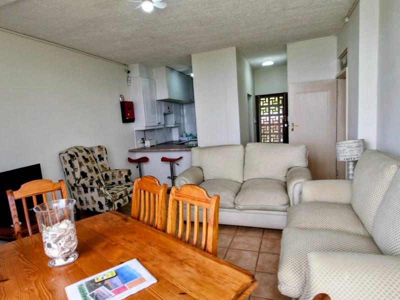 Open plan living and dining area featuring tiled flooring and a compact kitchen with built-in cabinetry and breakfast bar.