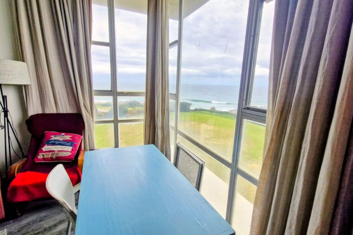 A living area featuring expansive floor-to-ceiling windows that offer panoramic ocean and coastal views, providing ample natural light.