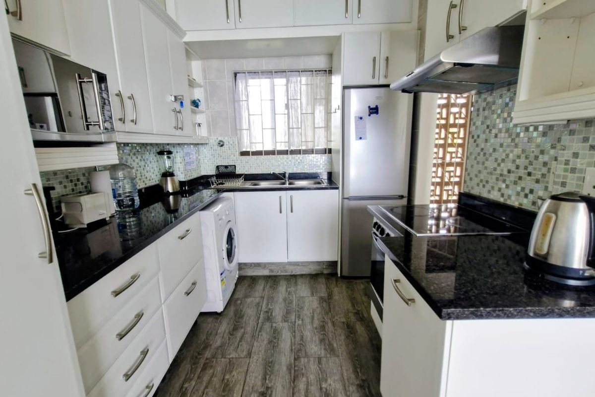 A functional kitchen featuring white cabinetry, dark granite countertops, a tiled backsplash, and integrated appliances including an oven and extractor fan.