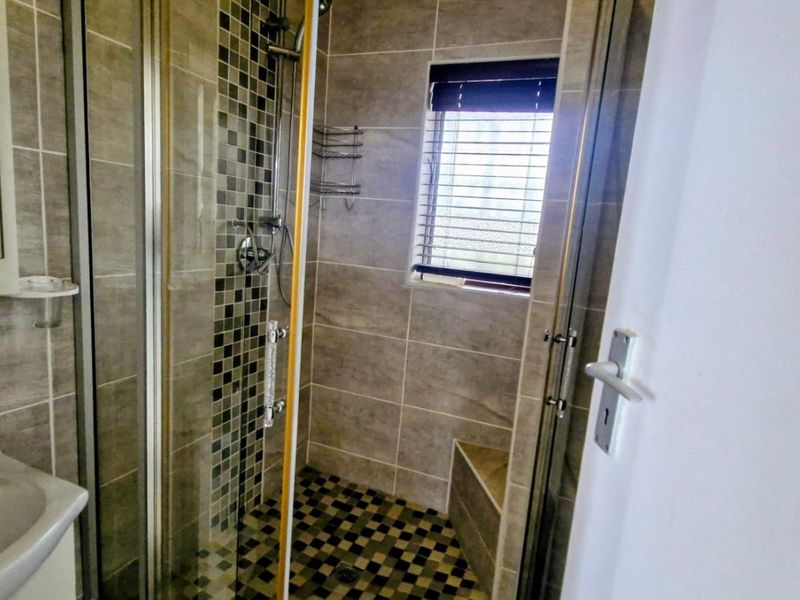 A modern bathroom featuring a tiled shower enclosure with a built-in bench, mosaic accent tiling, and a wall-mounted basin.