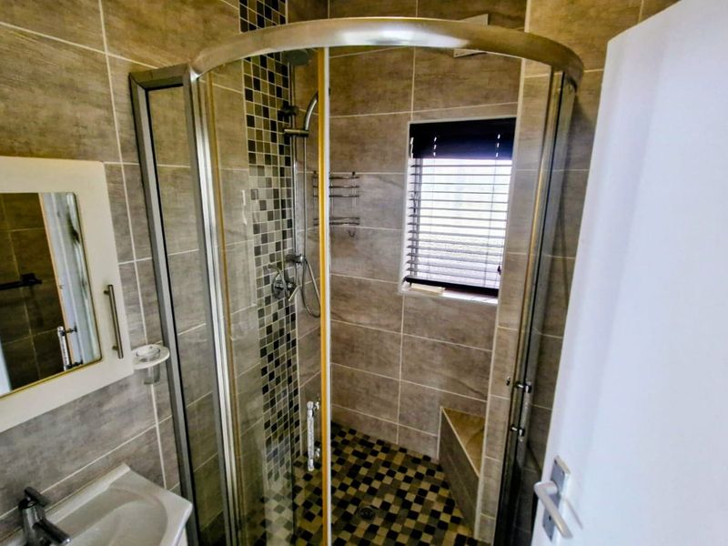 Modern bathroom featuring a curved glass shower enclosure with mosaic tile accents, built-in shower bench, and neutral wall tiling.