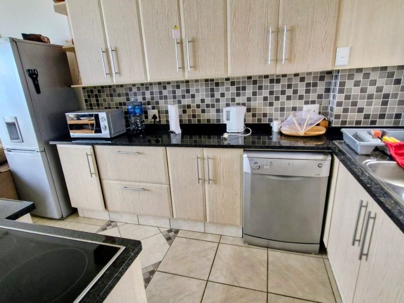 A functional kitchen featuring light wood-finish cabinetry, dark granite countertops, a mosaic tile backsplash, and a double bowl stainless steel sink.