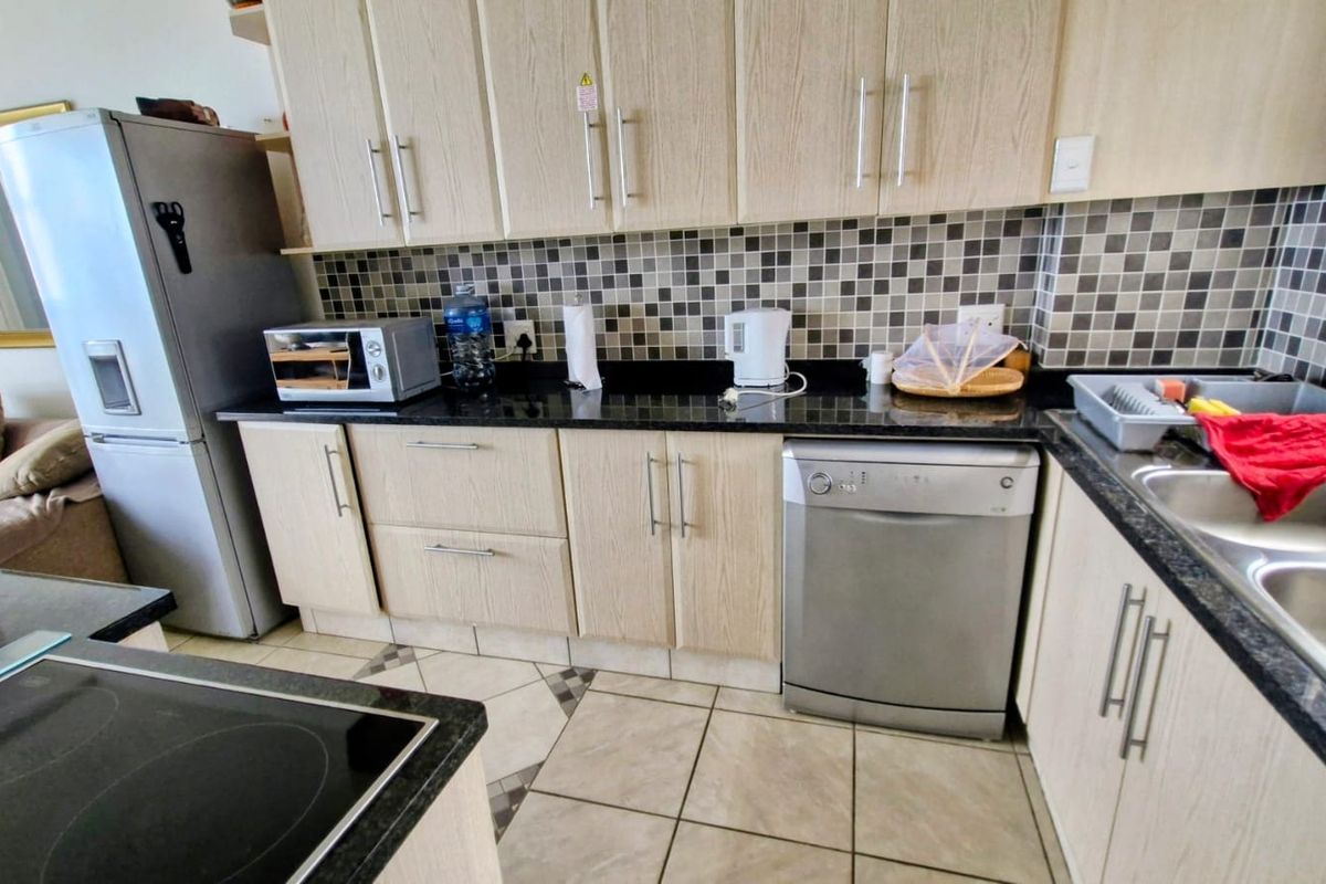 A functional kitchen featuring light wood-finish cabinetry, dark granite countertops, a mosaic tile backsplash, and a double bowl stainless steel sink.