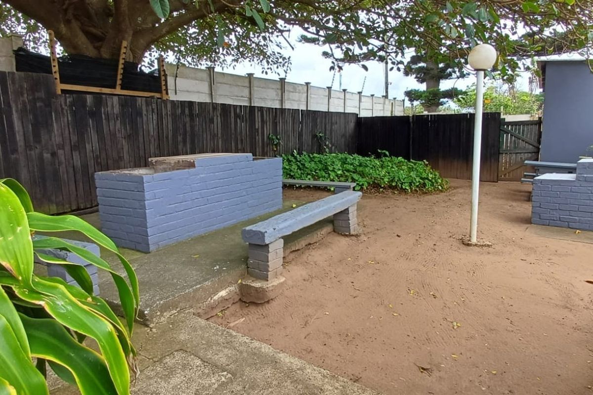 Rear outdoor area featuring built-in brick braai facilities, concrete seating, and perimeter fencing, offering potential for landscaping and patio improvement.