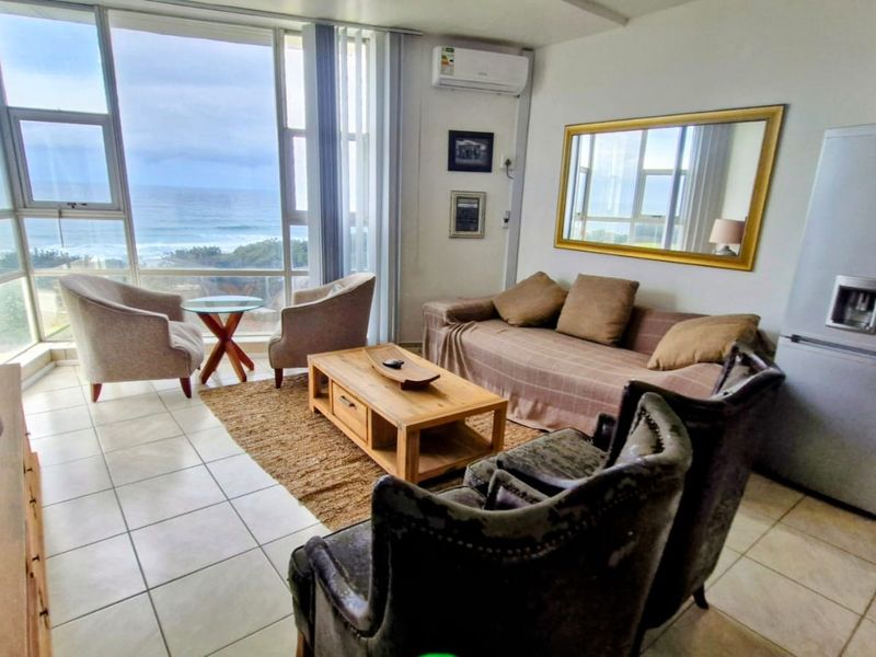 A bright living area featuring large floor-to-ceiling windows with ocean views, tiled flooring, and a wall-mounted air conditioning unit.