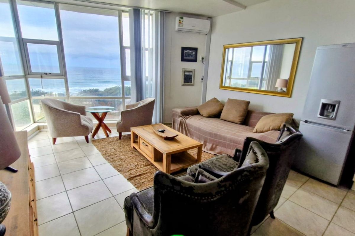 A bright living area featuring large floor-to-ceiling windows with ocean views, tiled flooring, and a wall-mounted air conditioning unit.