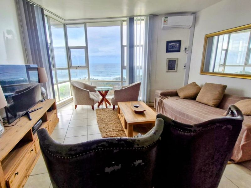 A bright living room featuring large windows with ocean views, tiled flooring, and a wall-mounted air conditioning unit.