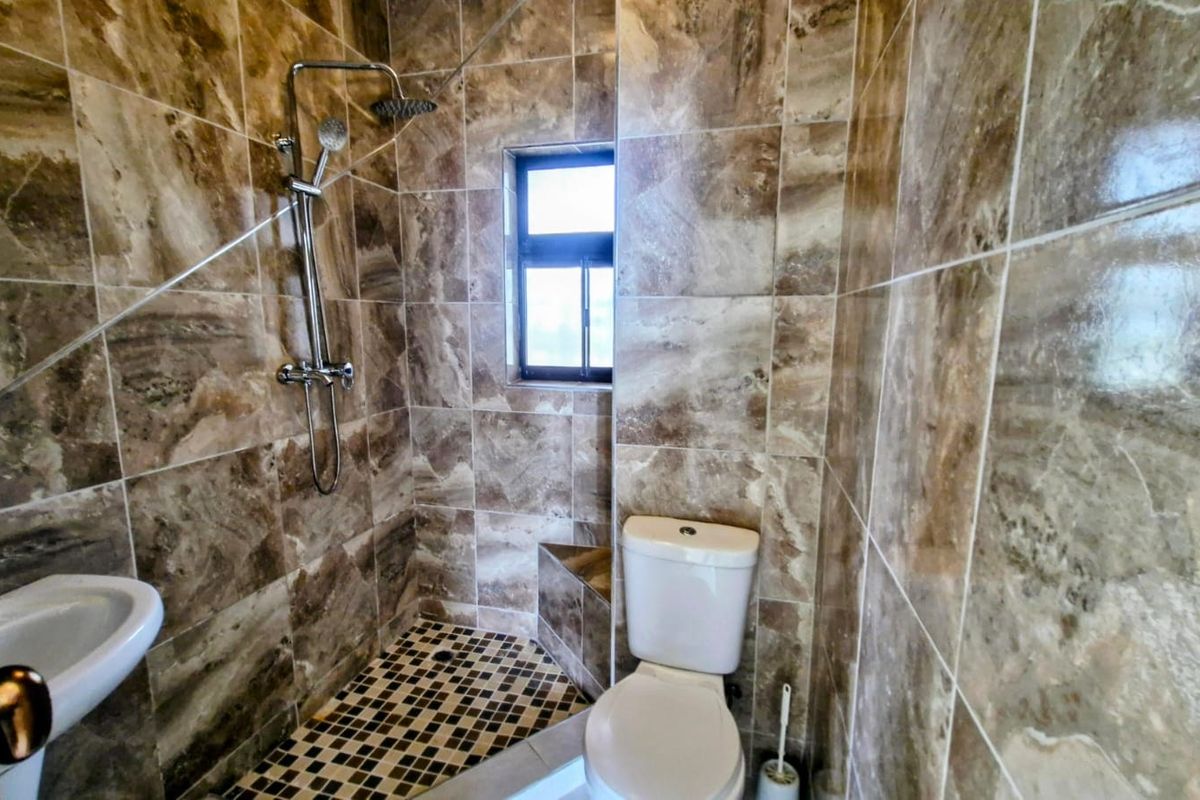 A compact bathroom featuring floor-to-ceiling marble-look wall tiles, a walk-in shower with a modern mixer, a white toilet, and a wall-mounted basin.