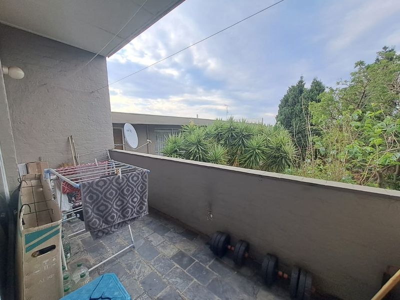 A functional balcony space featuring stone tile flooring and a concrete balustrade, offering an open outdoor area with views of surrounding greenery.