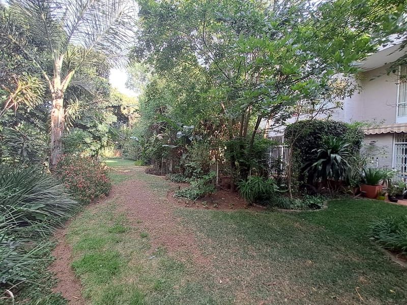 A private rear garden area featuring established trees, lush greenery, and a lawn, providing a peaceful outdoor space adjacent to the apartment building.