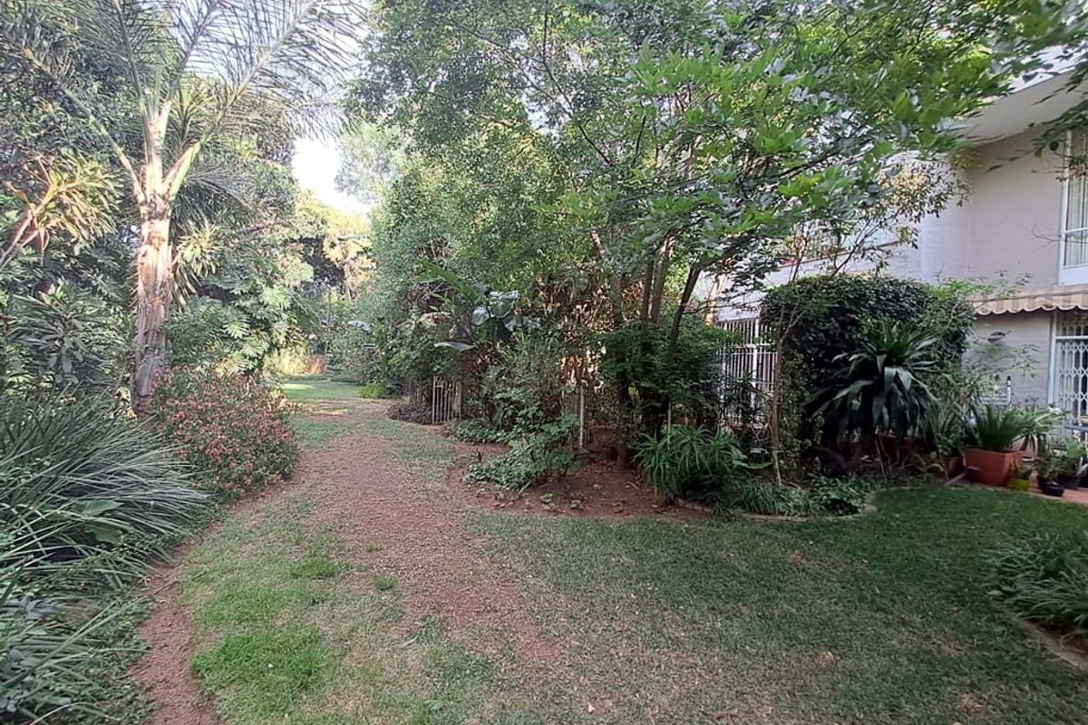 A private rear garden area featuring established trees, lush greenery, and a lawn, providing a peaceful outdoor space adjacent to the apartment building.