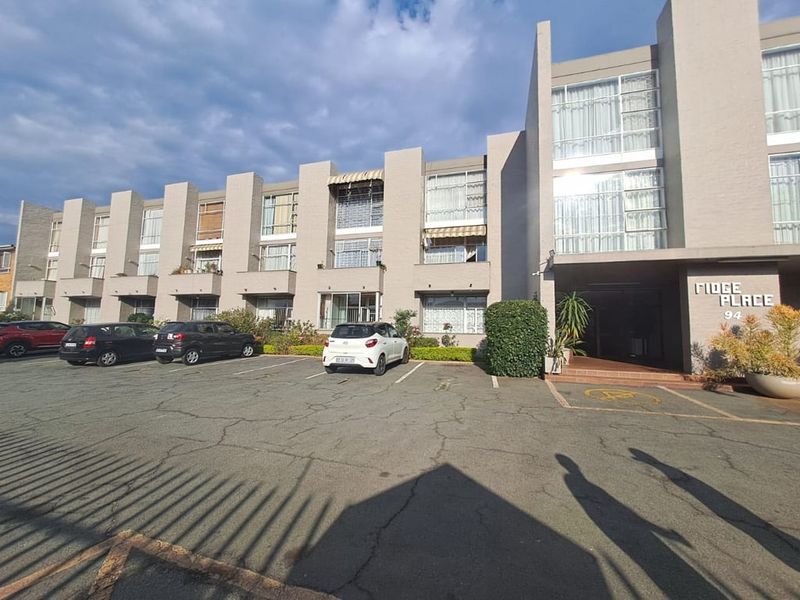 Front exterior view of Fidge Place apartment complex featuring a multi-story facade with large windows and an asphalt parking area.
