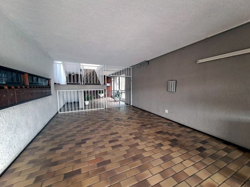 A spacious, empty apartment entrance lobby featuring tiled flooring, built-in mailboxes, and metal security gate access to the stairwell.