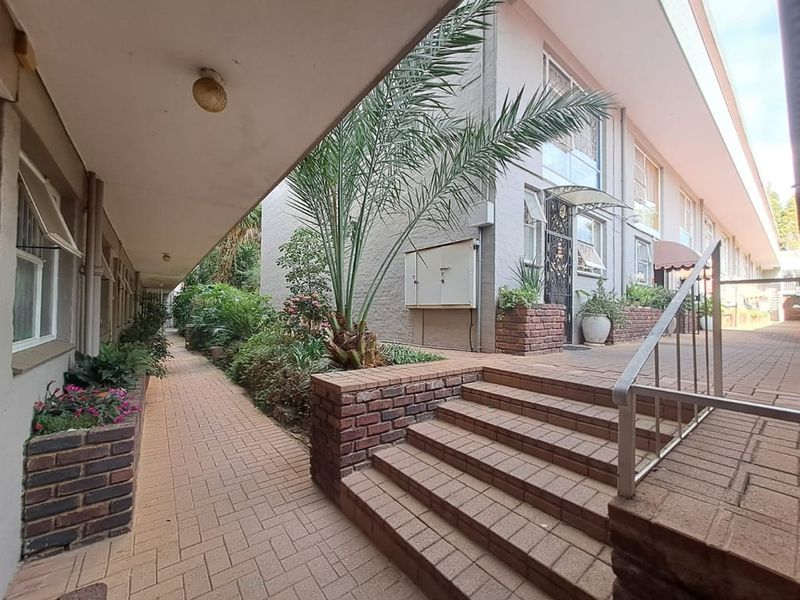 A well-maintained exterior walkway featuring brick paving, tiered brick retaining walls, and metal handrails leading to the apartment entrance.