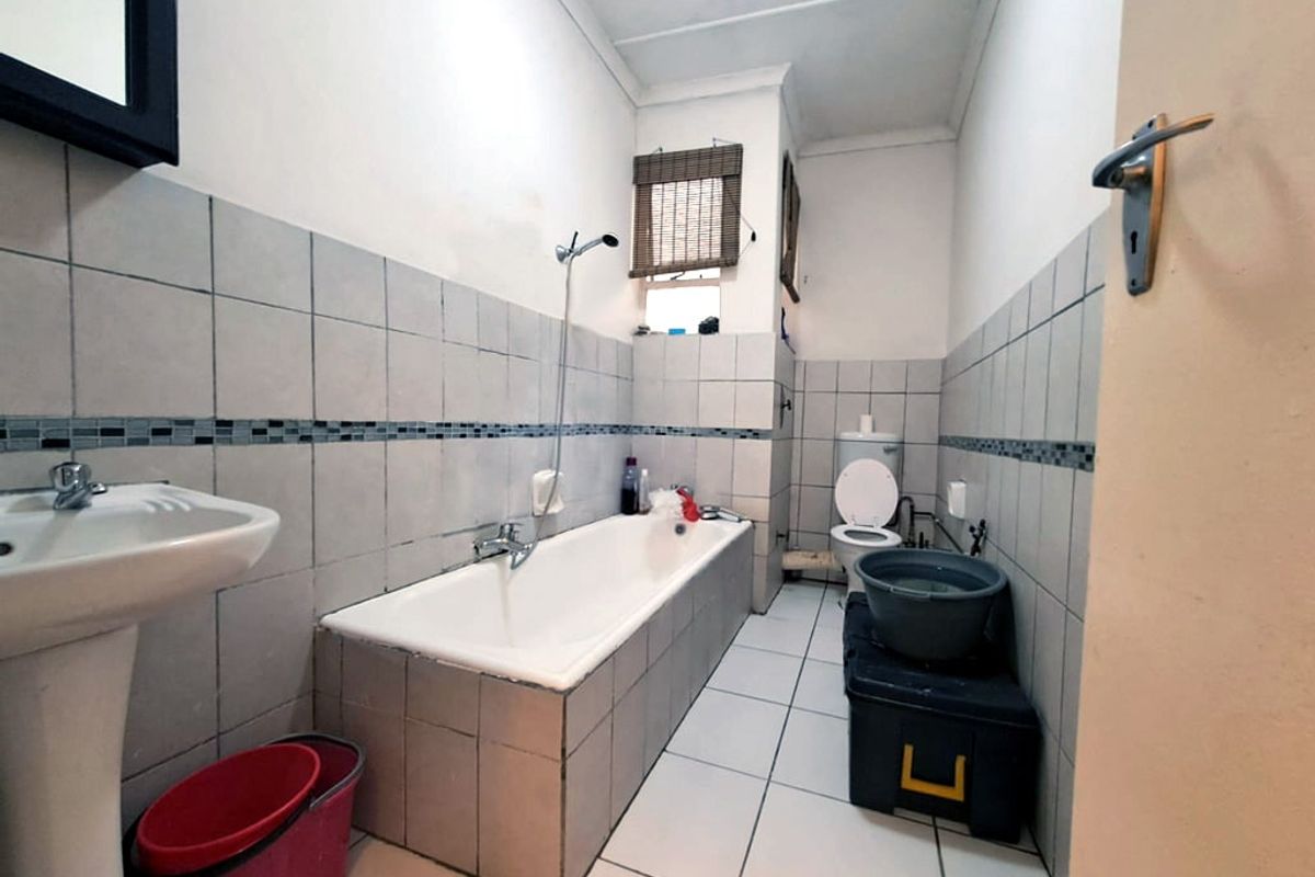 A functional bathroom featuring a pedestal basin, built-in bathtub with shower mixer, and a toilet, finished with neutral ceramic wall and floor tiles.