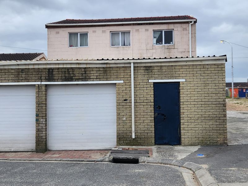 Front view of a double garage with brick facade and a second-story residential section, showing signs of exterior wear and maintenance requirements.