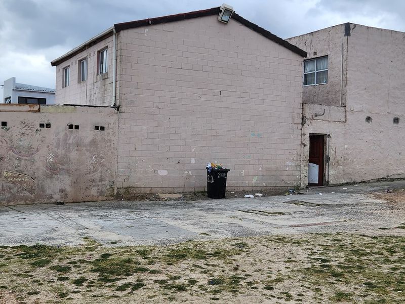 Rear exterior view of the property showing a concrete block structure, paved yard area, and perimeter wall with visible signs of weathering.