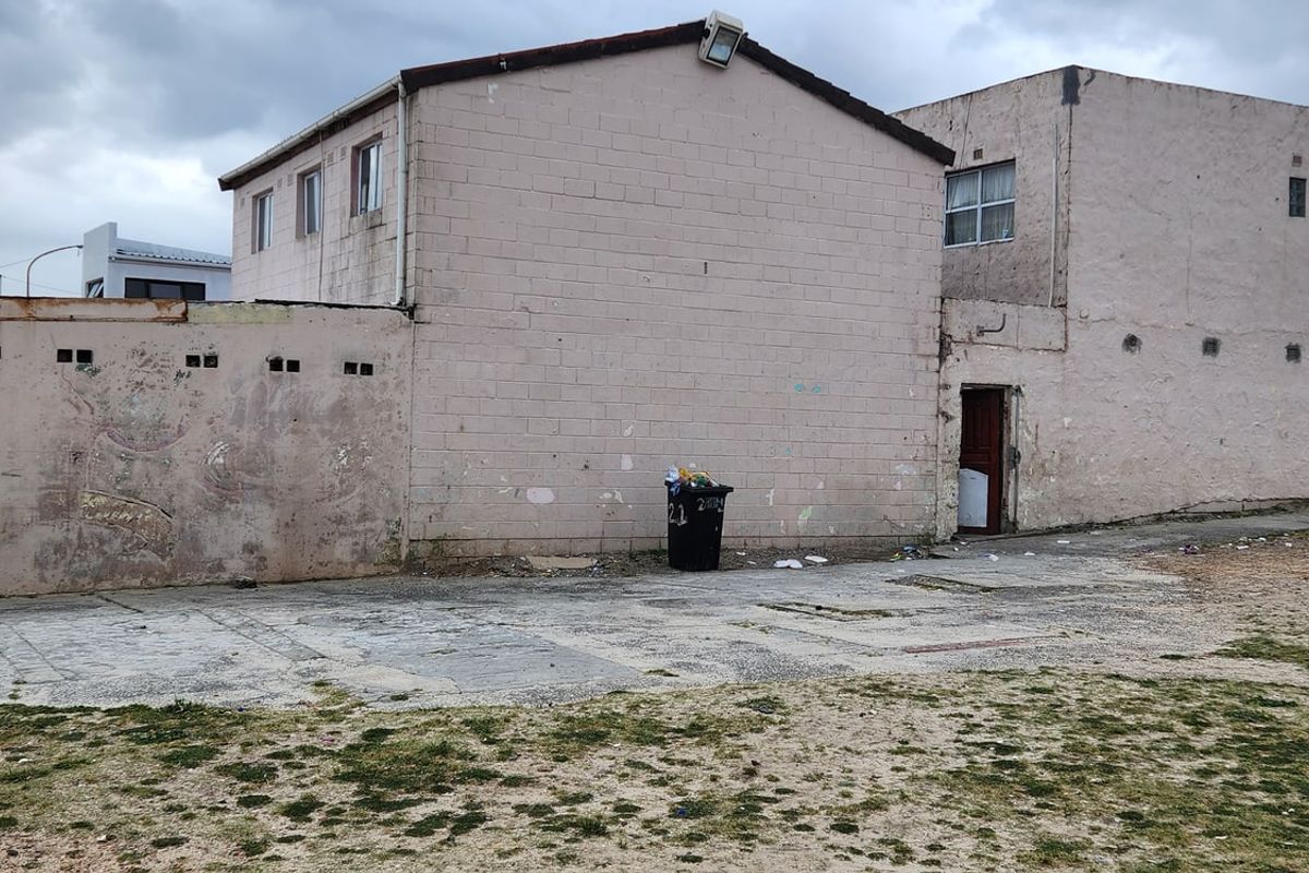 Rear exterior view of the property showing a concrete block structure, paved yard area, and perimeter wall with visible signs of weathering.
