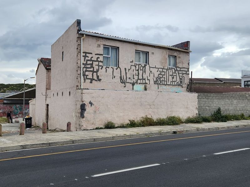 Street-facing view of a residential property featuring a weathered facade with significant graffiti and structural wear, situated along a public road.