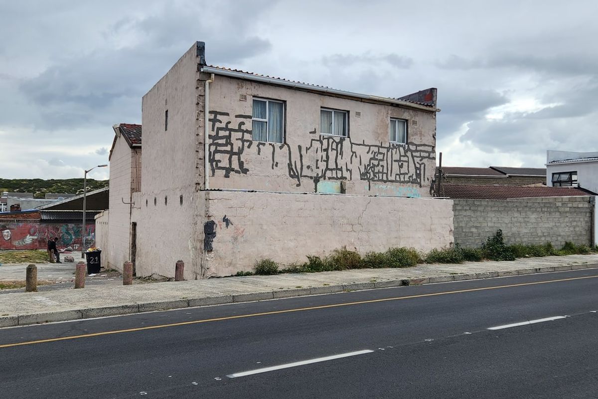 Street-facing view of a residential property featuring a weathered facade with significant graffiti and structural wear, situated along a public road.