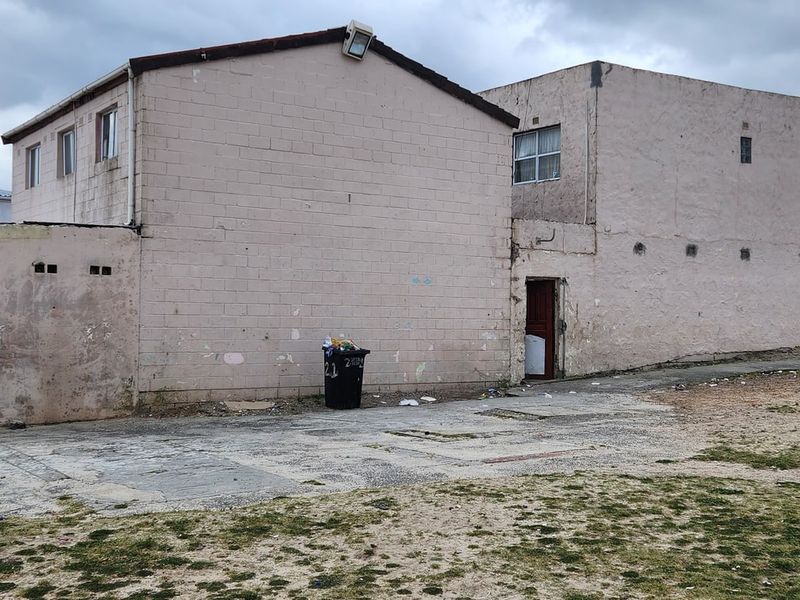 Rear view of a multi-story concrete block building featuring a paved yard area and weathered exterior wall finishes.