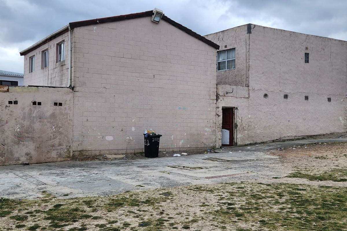 Rear view of a multi-story concrete block building featuring a paved yard area and weathered exterior wall finishes.