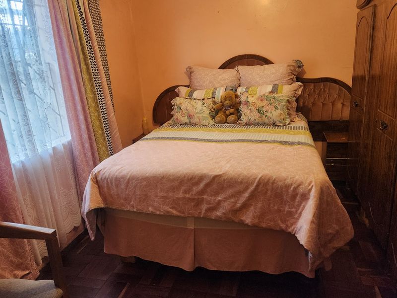 A bedroom featuring classic parquet flooring and a built-in headboard, currently requiring cosmetic updates to the wall finishes.