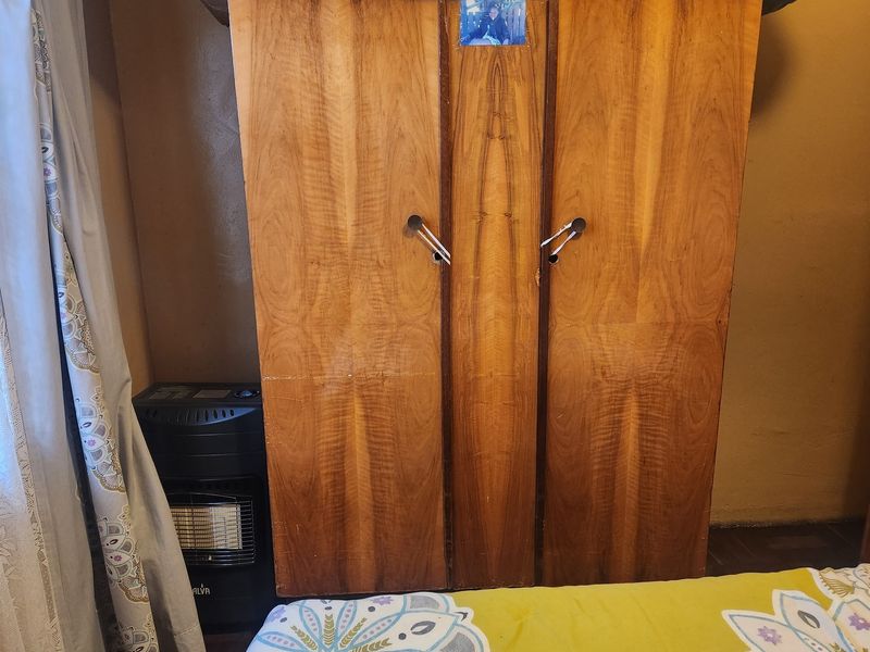A bedroom interior featuring a wooden wardrobe and basic wall finishes.