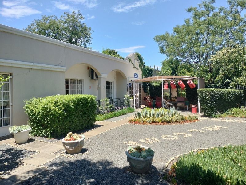 Rear exterior view featuring a gravel courtyard, landscaped garden beds, and a covered veranda area with wall-mounted air conditioning.