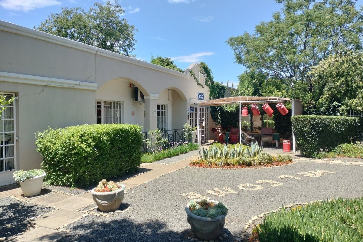 Rear exterior view featuring a gravel courtyard, landscaped garden beds, and a covered veranda area with wall-mounted air conditioning.