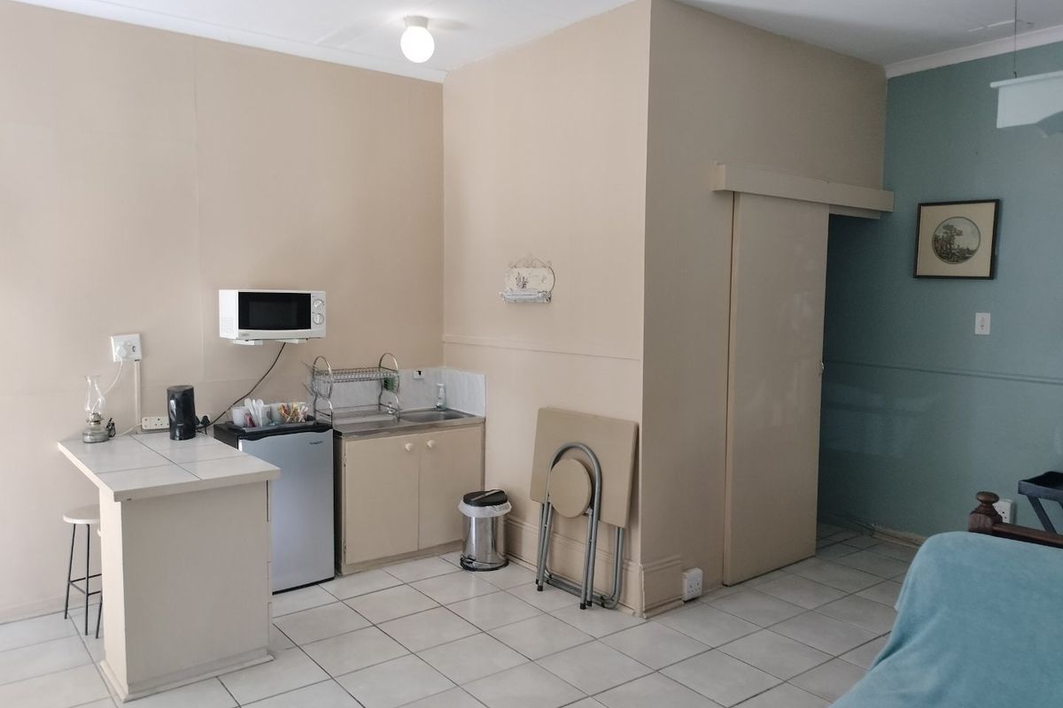 A compact kitchenette area featuring tiled flooring, built-in cabinetry, a stainless steel sink, and a tiled breakfast counter.
