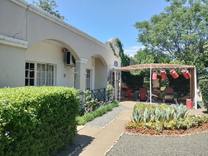 Front facade of the property featuring an arched veranda, paved walkway, and a well-maintained garden area with a metal pergola.