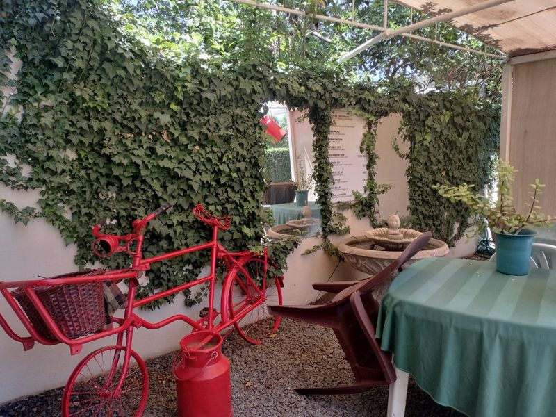A shaded outdoor patio area featuring a stone fountain, gravel flooring, and an ivy-covered wall.