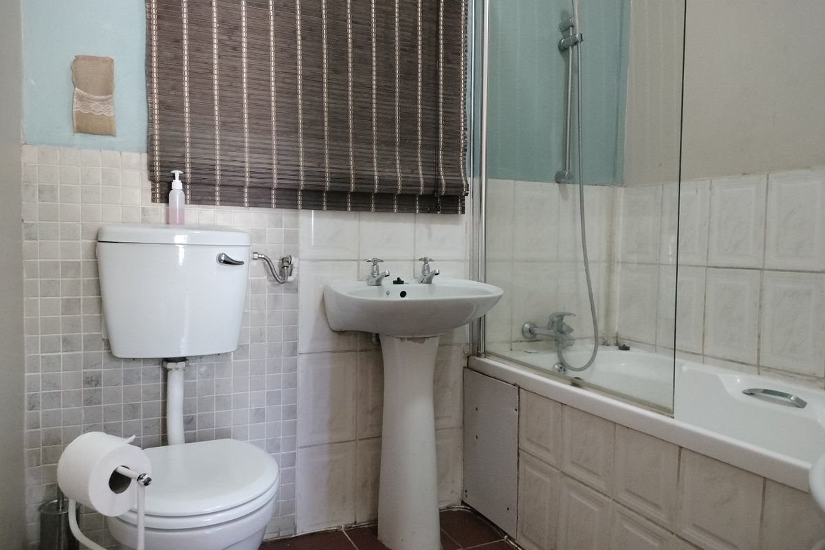 A functional bathroom featuring a pedestal basin, close-coupled toilet, and a bathtub with a glass shower screen, finished with wall and floor tiling.