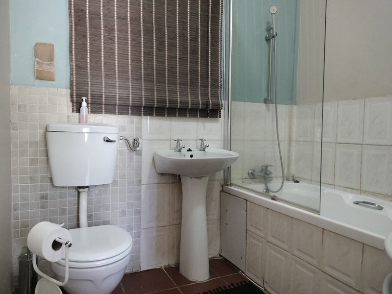 A functional bathroom featuring a pedestal basin, close-coupled toilet, and a bathtub with a glass shower screen, finished with wall and floor tiling.
