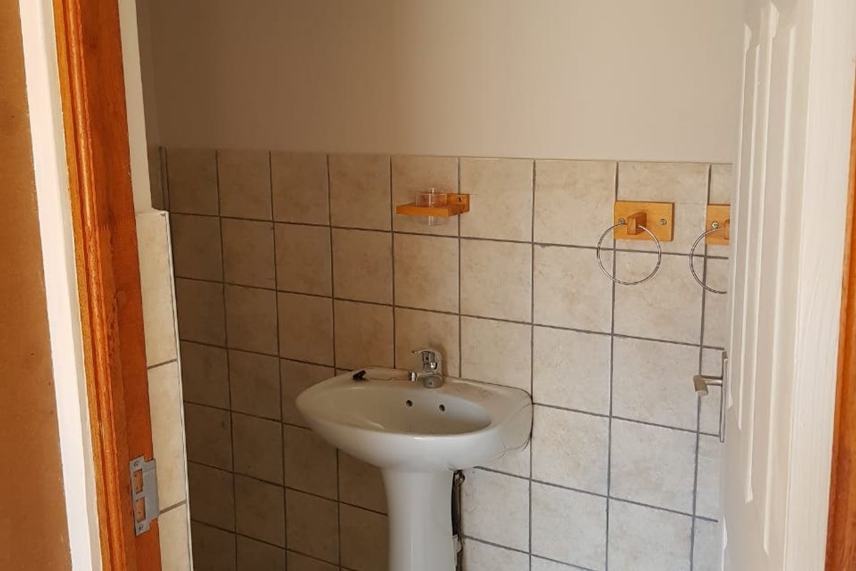 A compact guest bathroom featuring a pedestal basin and tiled splashback, currently in need of cosmetic updates.